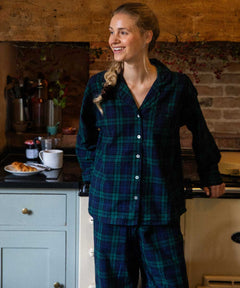 Woman in black watch tartan pyjamas standing in a kitchen.