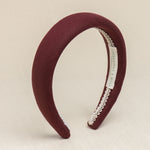 A burgundy colored headband made of linen, displayed on a neutral background.