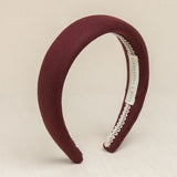 A burgundy colored headband made of linen, displayed on a neutral background.