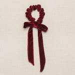 A red velvet scrunchie with an attached hair bow, displayed on a neutral background.