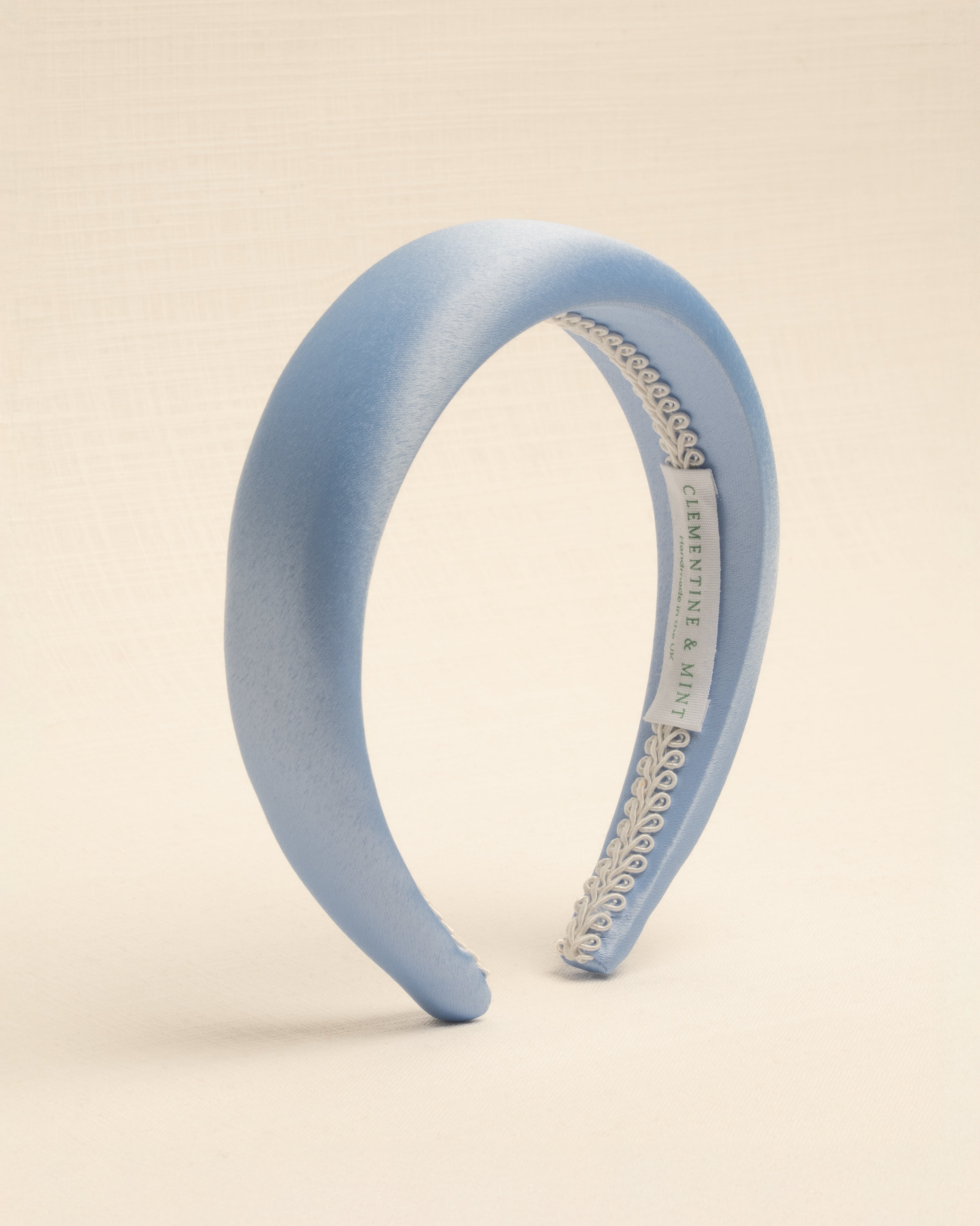 A light blue satin headband with a visible brand label on the inside, displayed against a neutral background.