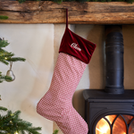 Red checkered Christmas stocking with velvet top hanging by a fireplace.