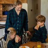 Woman and two children in a kitchen setting wearing matching black watch tartan pyjamas
