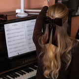 Person with long blonde hair and a brown velvet bow sitting at a piano.