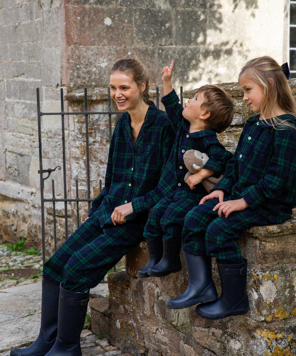 Family of three wearing matching black watch plaid pyjamas sitting on stone steps.