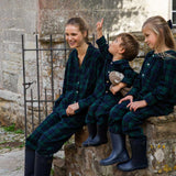 Family of three wearing matching black watch plaid pyjamas sitting on stone steps.