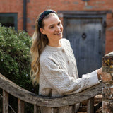 Woman wearing a tartan headband and cream cable knit sweater sitting on a wooden bench outdoors.