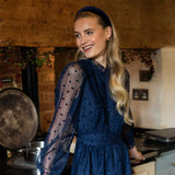 Woman in a blue dress and blue velvet headband standing in a rustic kitchen.