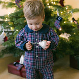 A child in a Christmas-themed brushed cotton tartan pyjama set with a contrasting Peter Pan collar, standing in front of a Christmas tree.