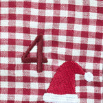 A close-up of a red and white gingham fabric surface with an embroidered red number 4 and a red Santa hat with a white pom-pom.