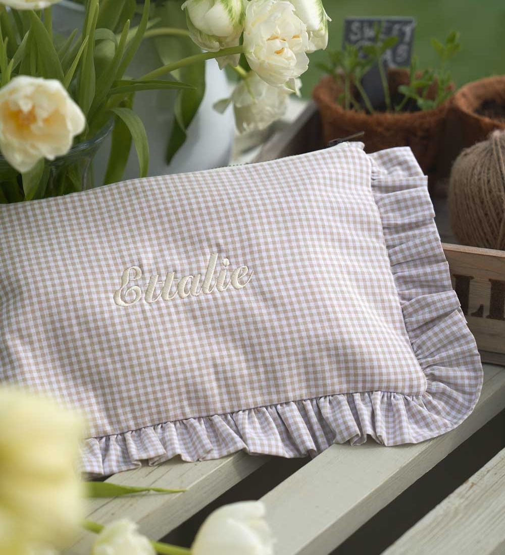 Gingham ruffle pouch with 'Ettalie"embroidery on a table with flowers and plants.