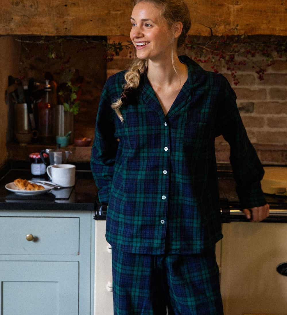 Woman in black watch tartan pyjamas standing in a kitchen.