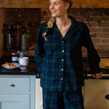 Woman in black watch tartan pyjamas standing in a kitchen.