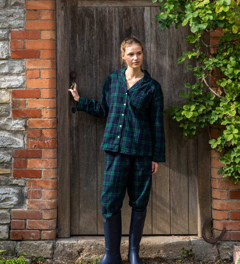 Woman in black watch tartan winter pyjamas standing in front of a wooden door.