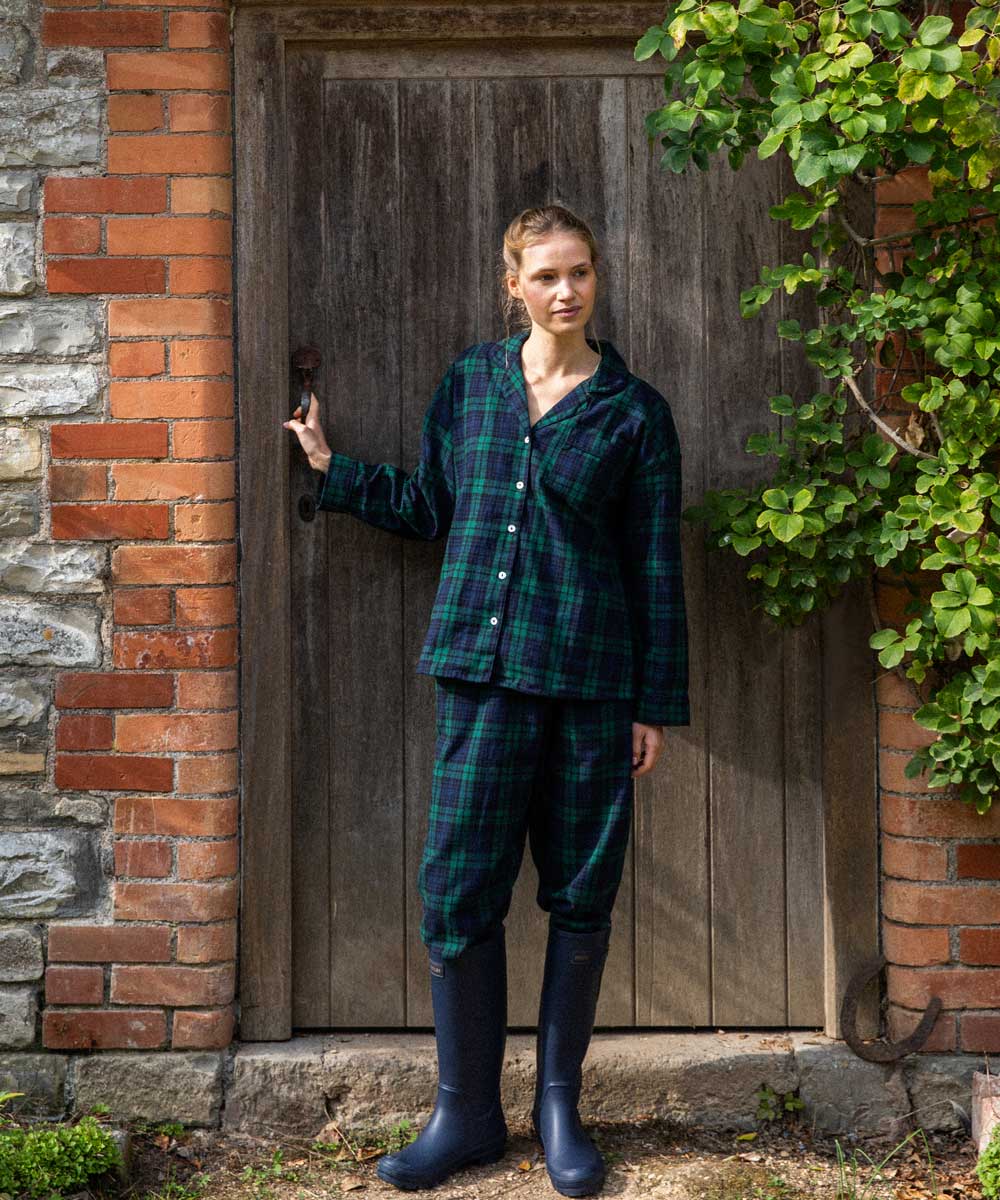 Woman in black watch tartan winter pyjamas standing in front of a wooden door.