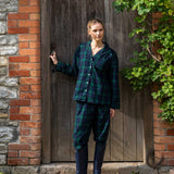 Woman in black watch tartan winter pyjamas standing in front of a wooden door.
