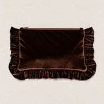 A dark brown velvet clutch bag with ruffled trim on the sides and bottom, featuring a top zipper closure, set against a light beige textured background.