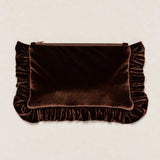 A dark brown velvet clutch bag with ruffled trim on the sides and bottom, featuring a top zipper closure, set against a light beige textured background.