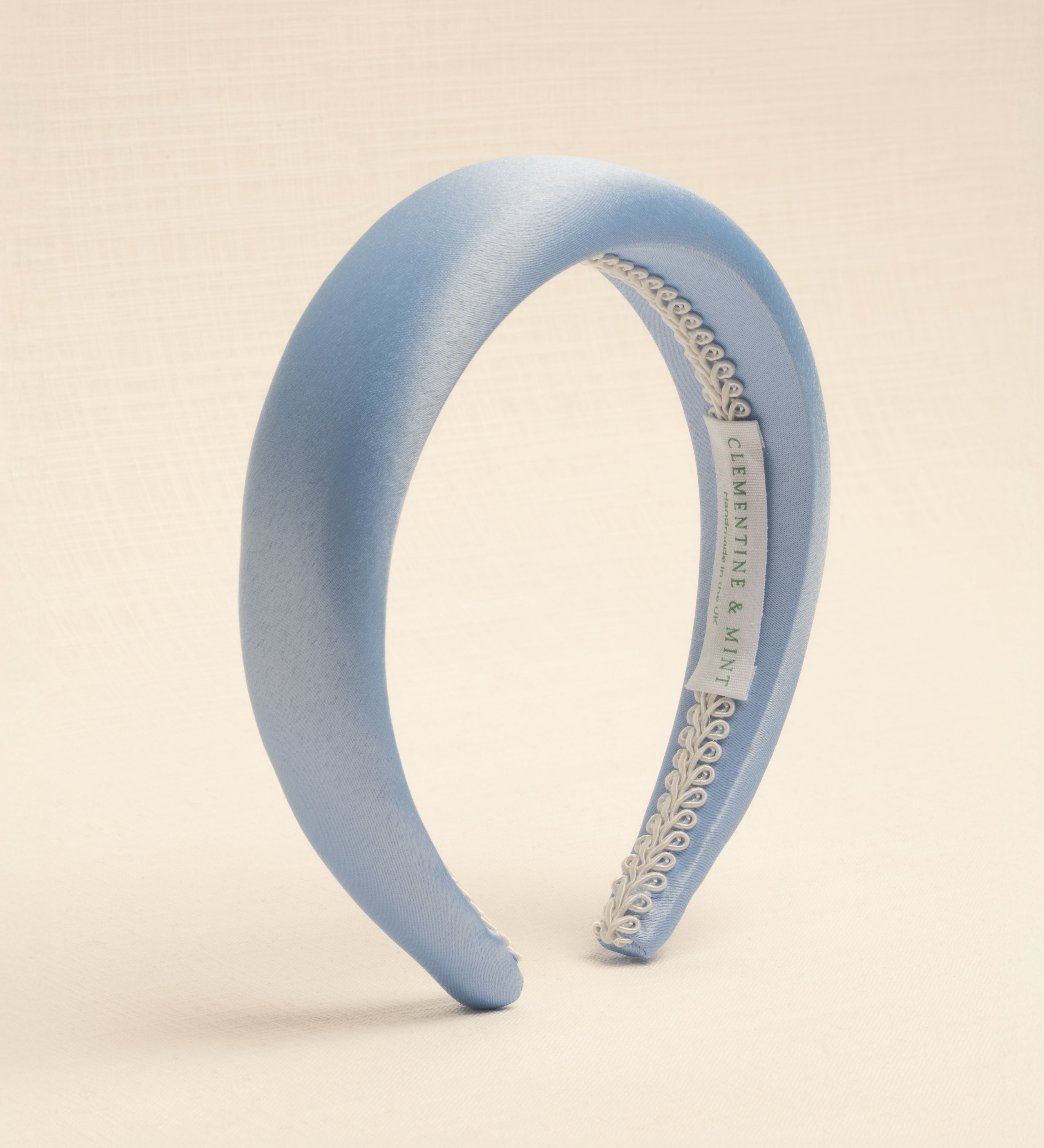 A light blue satin headband with a visible brand label on the inside, displayed against a neutral background.