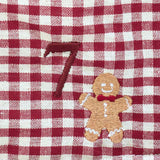 Close-up of a red and white gingham checkered fabric with an embroidered brown number 7 and a small gingerbread man motif.