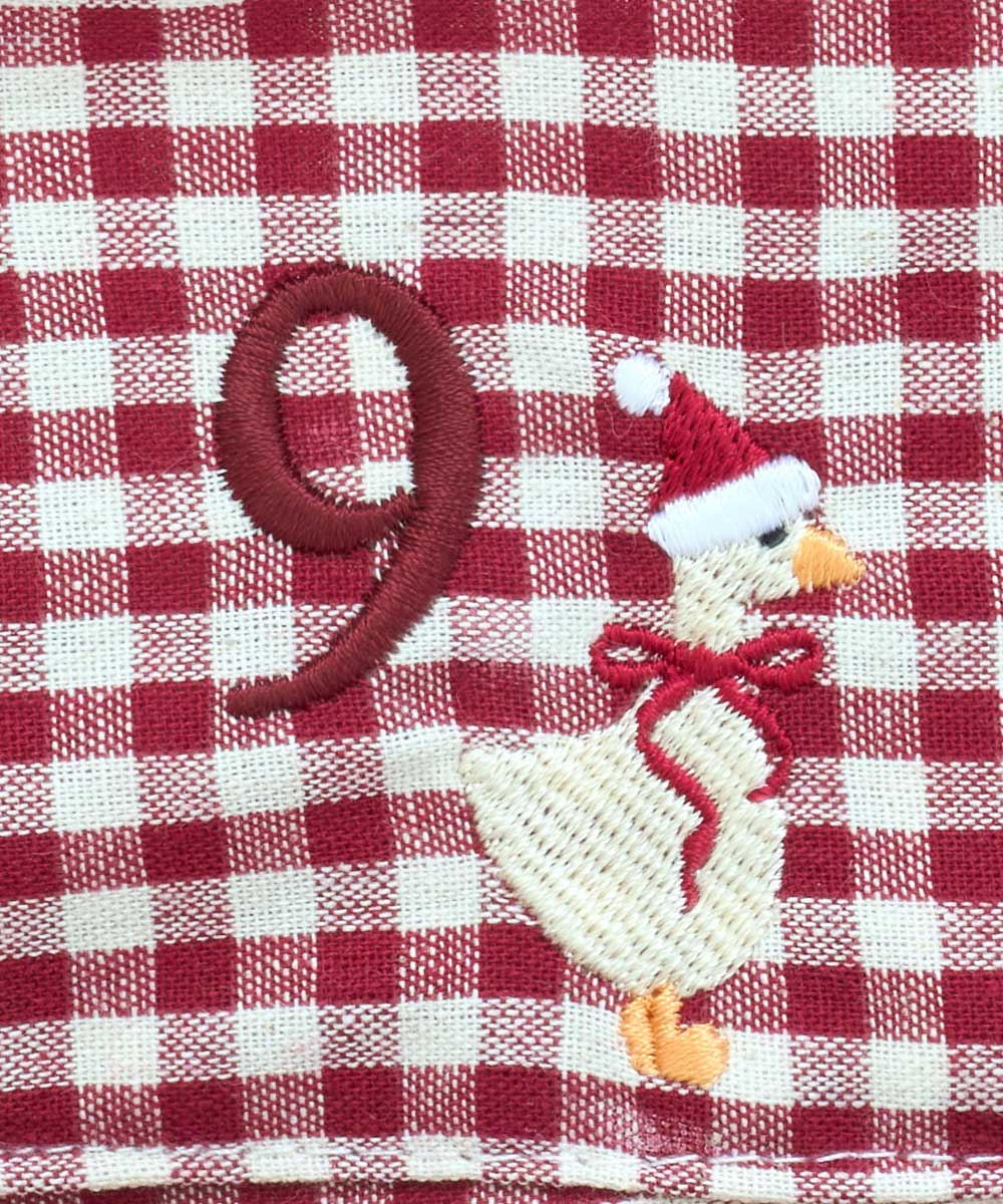 A close-up of a red and white gingham fabric surface featuring an embroidered design of a goose wearing a Santa hat and scarf next to a large red number 9.