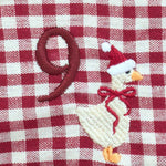 A close-up of a red and white gingham fabric surface featuring an embroidered design of a goose wearing a Santa hat and scarf next to a large red number 9.