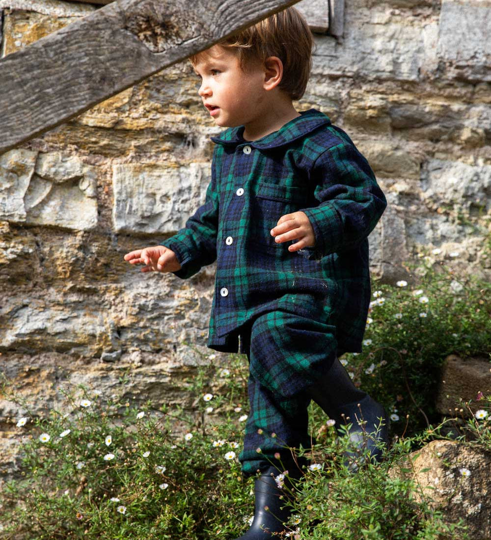 Child in a black watch tartan winter pyjamas standing outside 