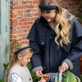 Woman and child outdoors with a basket of vegetables against a brick wall wearing navy tartan headbands 