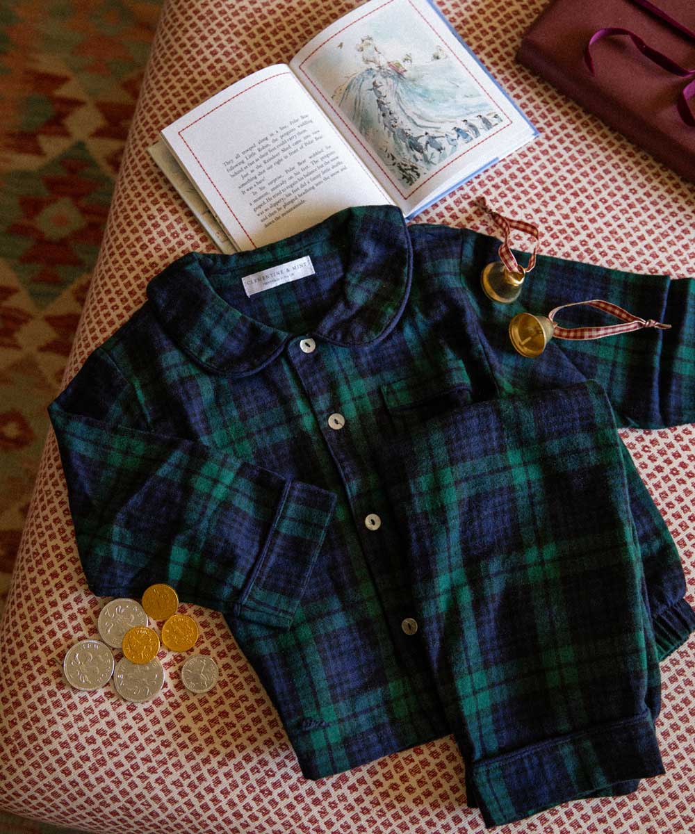 Plaid children's pyjamas with buttons on a textured surface next to an open book.