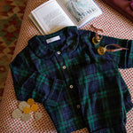 Plaid children's pyjamas with buttons on a textured surface next to an open book.