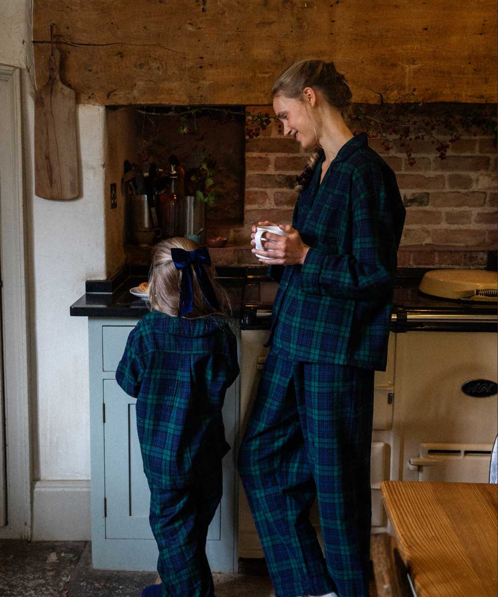 Woman and child in matching black watch tartan plaid pyjamas standing in a kitchen.