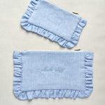Two light blue pouches with ruffled edges on a beige background