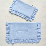 Two light blue pouches with ruffled edges on a beige background