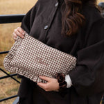 A person outdoors holding a brown and beige gingham clutch bag with the name 'chloe' embroidered on the front. The person is wearing a dark brown coat.