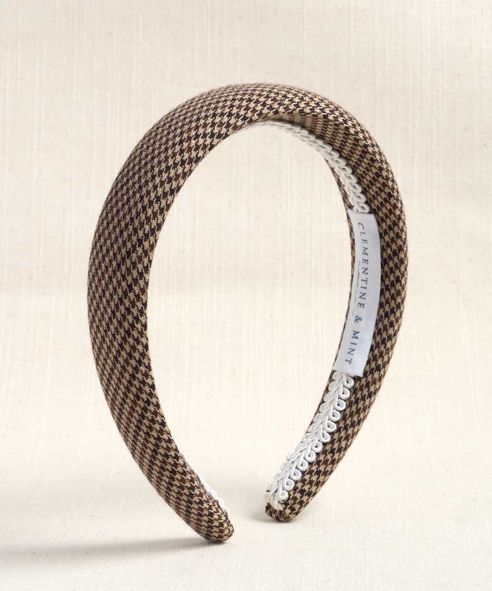 A wide headband with a brown and beige houndstooth pattern, finished with a white trim on one side and a white interior label reading 'CLEMENTINE & MINE'.