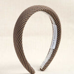 A wide headband with a brown and beige houndstooth pattern, finished with a white trim on one side and a white interior label reading 'CLEMENTINE & MINE'.