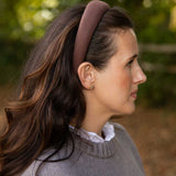 A woman in profile wearing a wide, brown headband and a gray knit sweater, photographed outdoors with a soft blurred green and brown background.
