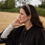 A woman in a black coat and white long-sleeve shirt wearing a brown patterned headband, posing outdoors in a field.