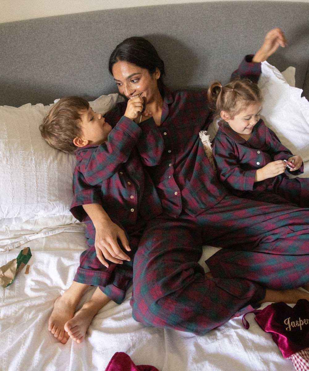 children and mum wearing matching burgundy tartan pyjamas on a bed opening presents 