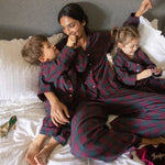children and mum wearing matching burgundy tartan pyjamas on a bed opening presents 