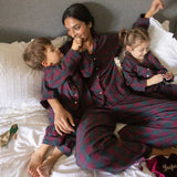 children and mum wearing matching burgundy tartan pyjamas on a bed opening presents 