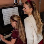 Woman and young girl playing piano together, smiling wearing burgundy velvet headbands