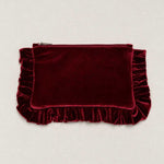 A deep burgundy velvet clutch pouch with a top zipper and decorative ruffled trim on the sides and bottom, displayed flat against a light beige background.
