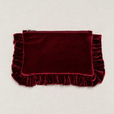 A deep burgundy velvet clutch pouch with a top zipper and decorative ruffled trim on the sides and bottom, displayed flat against a light beige background.