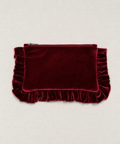 A deep burgundy velvet clutch pouch with a top zipper and decorative ruffled trim on the sides and bottom, displayed flat against a light beige background.