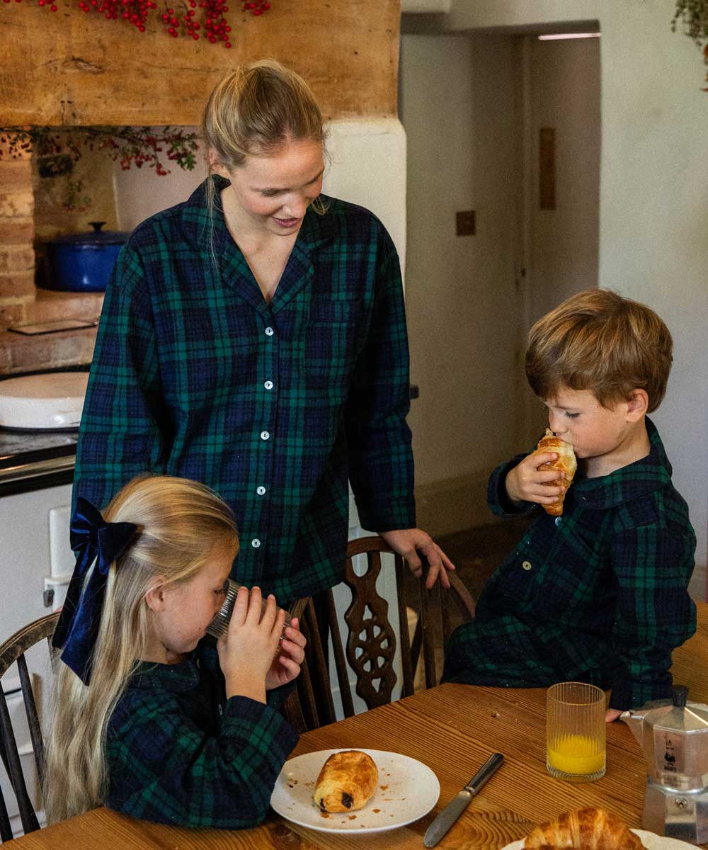 Woman and two children in a kitchen setting wearing matching black watch tartan pyjamas 