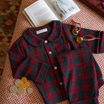 Childrens burgundy tartan pyjamas laid out on fabric with bells and a book 