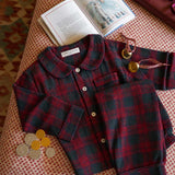 Childrens burgundy tartan pyjamas laid out on fabric with bells and a book 