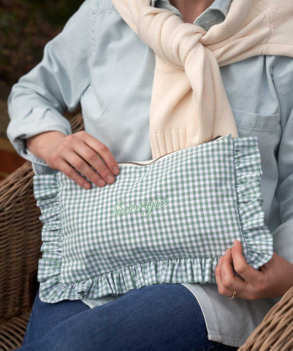 Person holding a green and white checkered ruffled pouch with 'Georgie' embroidery.