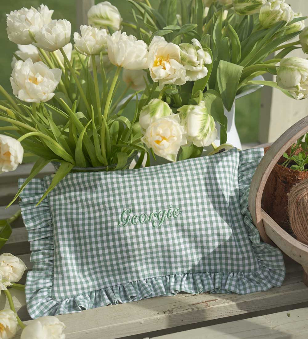 Green checkered ruffled pouch with 'Georgia' embroidery surrounded by white tulips on a wooden surface.